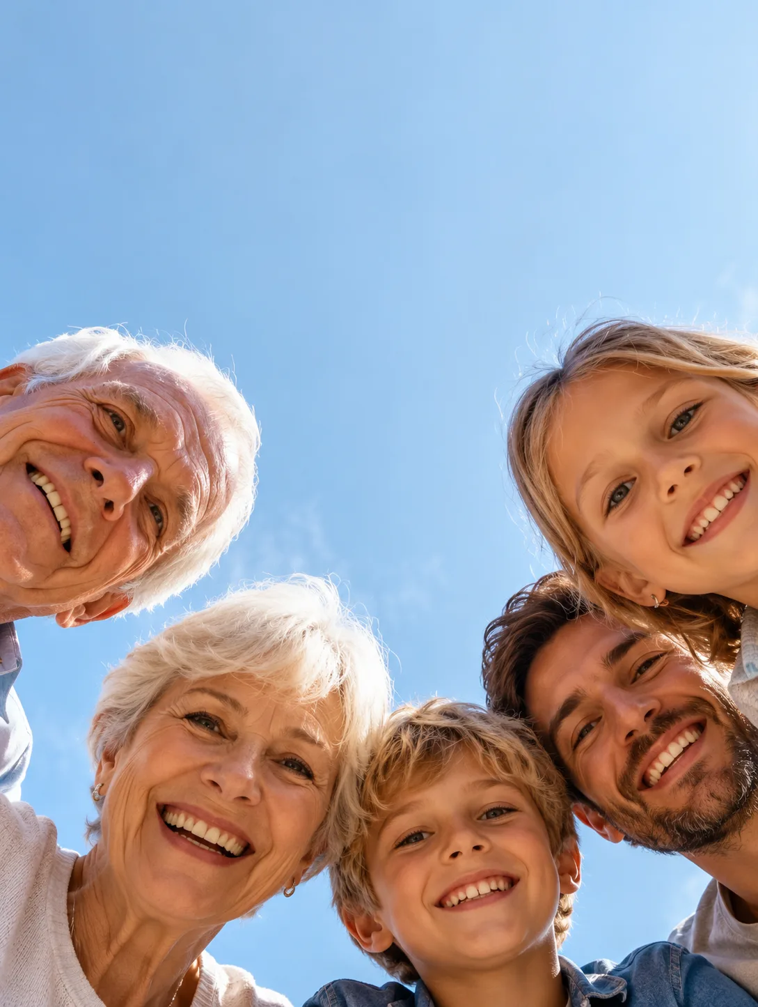A three-generation family smiling down at the camera against a blue sky.